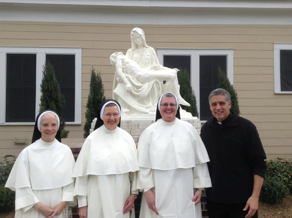 Father Mark Beard with three Dominican sisters beside a Pietà statue